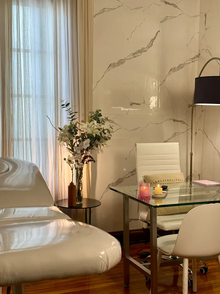 Consultorio con camilla, escritorio de vidrio y flores junto a la ventana